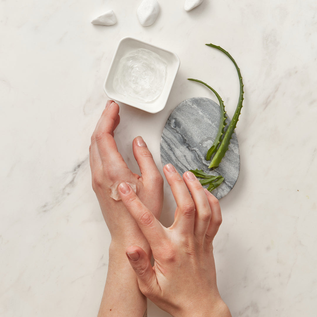 Image of hands applying a clear gel with aloe placed on a stone